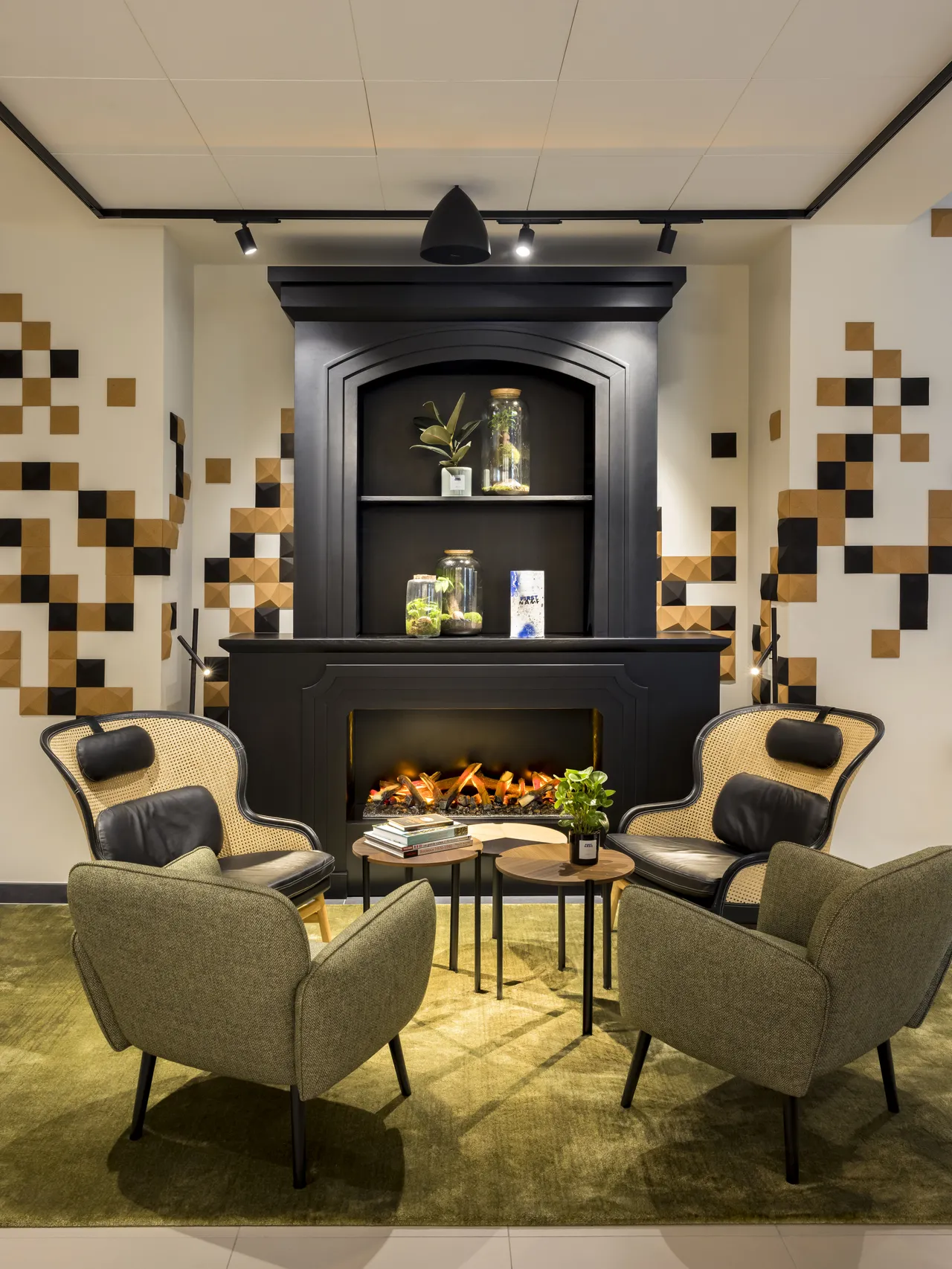 Modern lounge area with four grey armchairs surrounding a black side table, facing an electric fireplace set in black cabinetry, framed by geometric ceramic tiles in beige, brown, and black tones