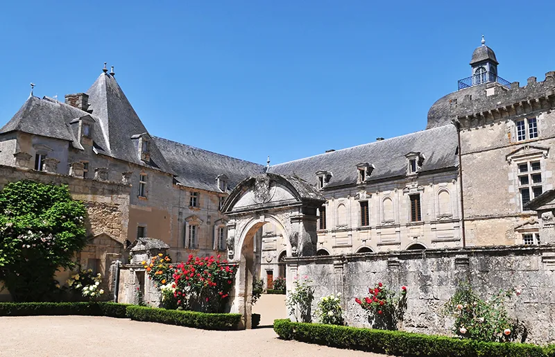 Inner courtyard of Château de Vayres near Bordeaux featuring medieval architecture, stone archway, crenellated towers and flowering gardens under clear sky.