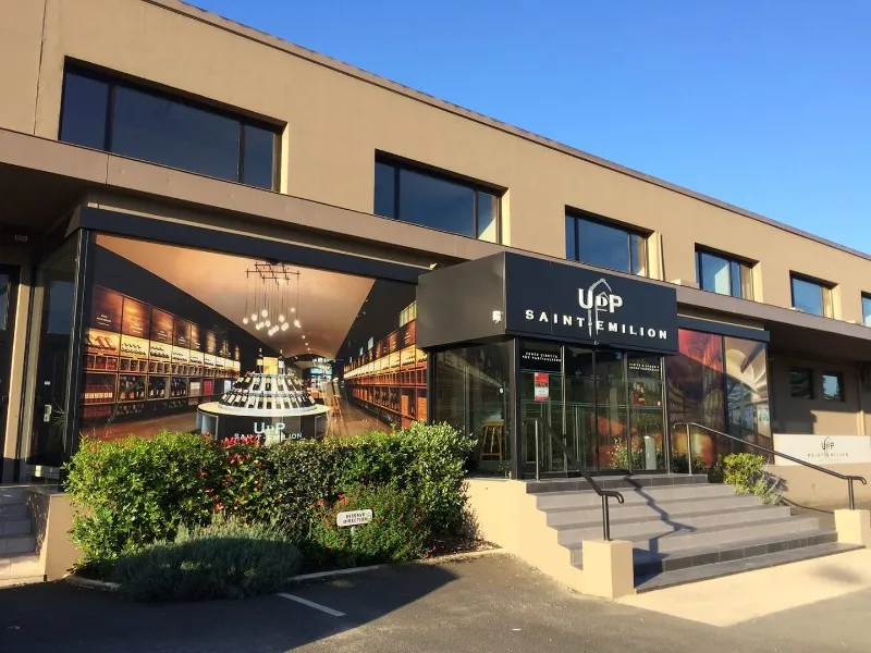 Modern storefront of Union of Saint-Emilion Producers in Bordeaux, featuring a wine bottle display window, stepped entrance and decorative plants