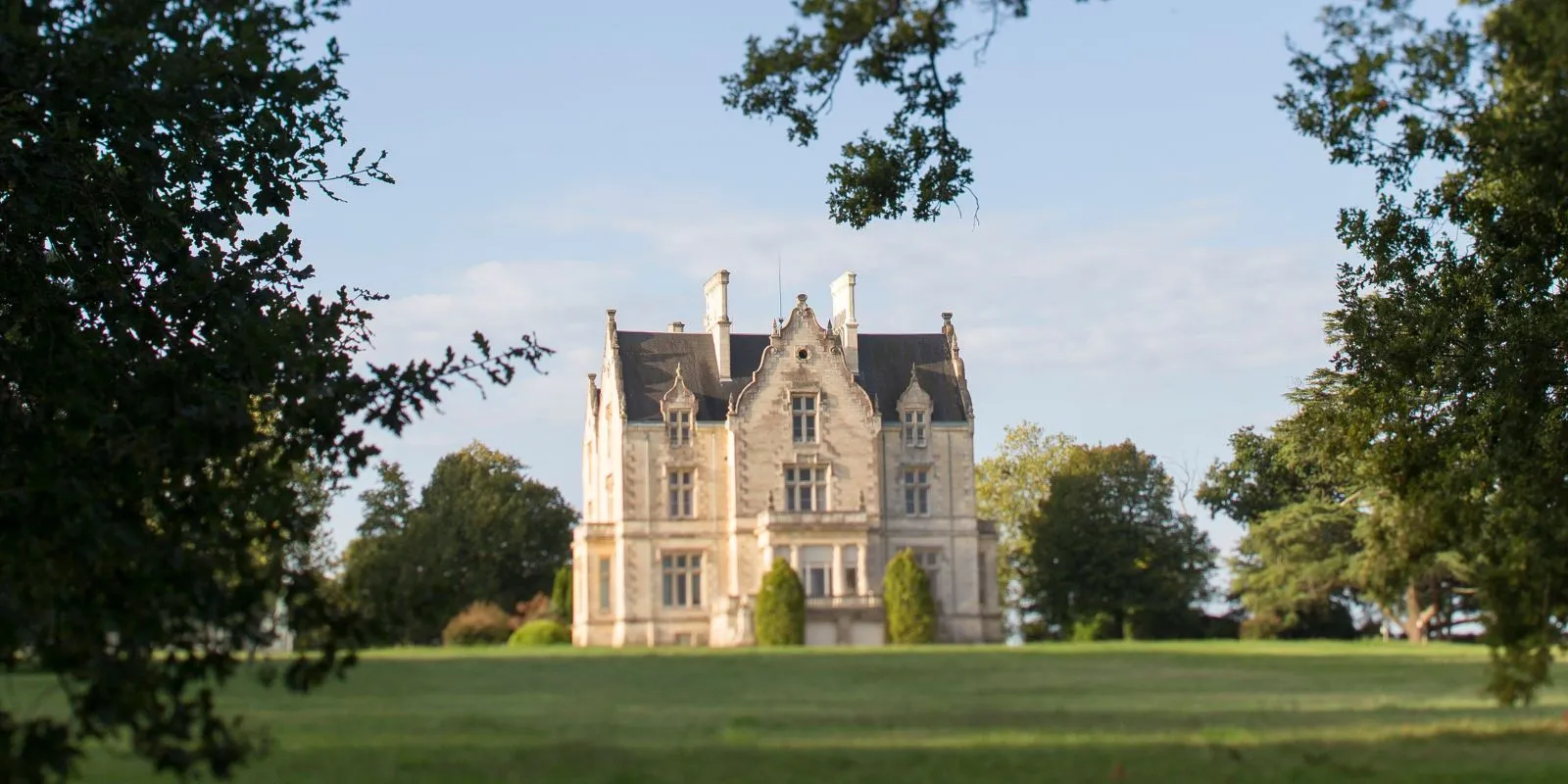 Château Lanessan, a 19th-century neo-gothic manor house surrounded by lush greenery and trees in the Bordeaux wine region.