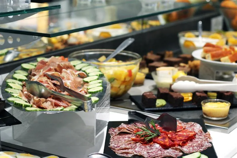 Assorted cold cuts platter featuring Parma ham and dry salami with fresh cucumber slices and pickles, displayed in a gourmet restaurant showcase in Bordeaux.
