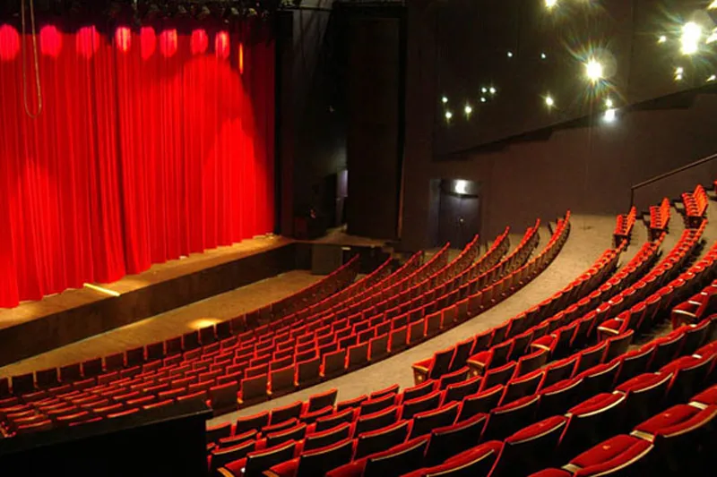 Interior of the National Theatre Bordeaux in Aquitaine showing rows of red seats facing a stage with red curtain and spotlight lighting.