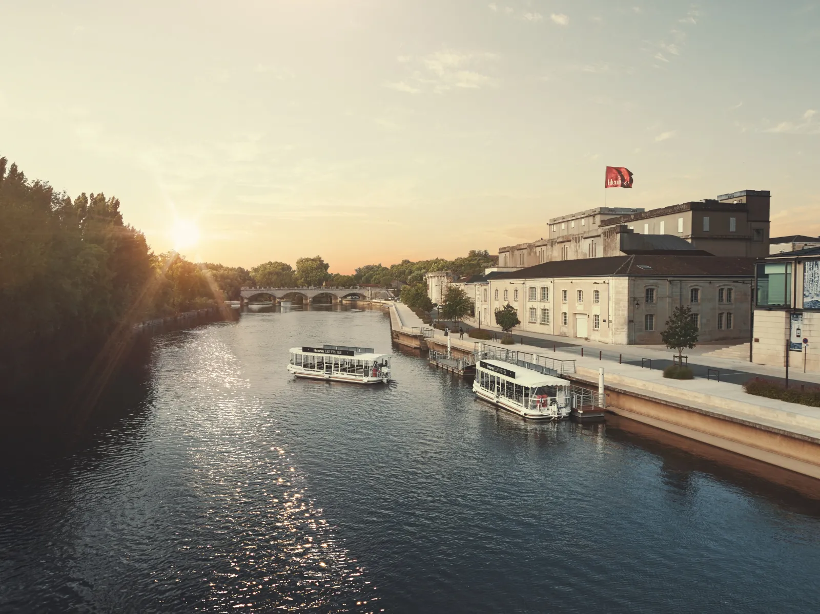 Sunset view of the Garonne River in Bordeaux with moored cruise boats, historic buildings, and a bridge in the background