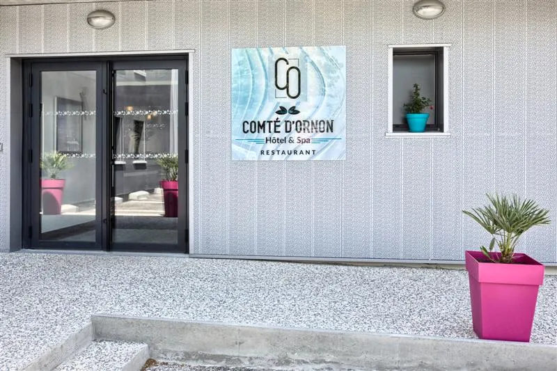 Comté d'Ornon hotel and spa restaurant facade in Bordeaux, featuring modern black glass doors, blue signage, and pink flower planters