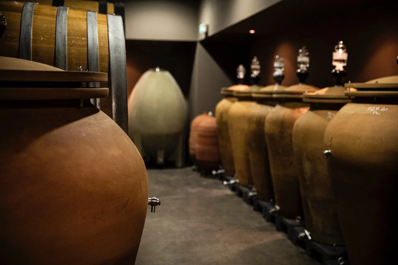 Row of oak barrels in the aging cellar of Château de Fieuzal in Bordeaux, featuring wooden casks and barrels lined up in warm ambient lighting.