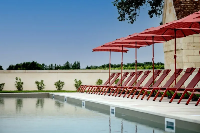 Outdoor swimming pool at Château Fage in Bordeaux featuring red lounge chairs under matching umbrellas on a modern terrace with white walls