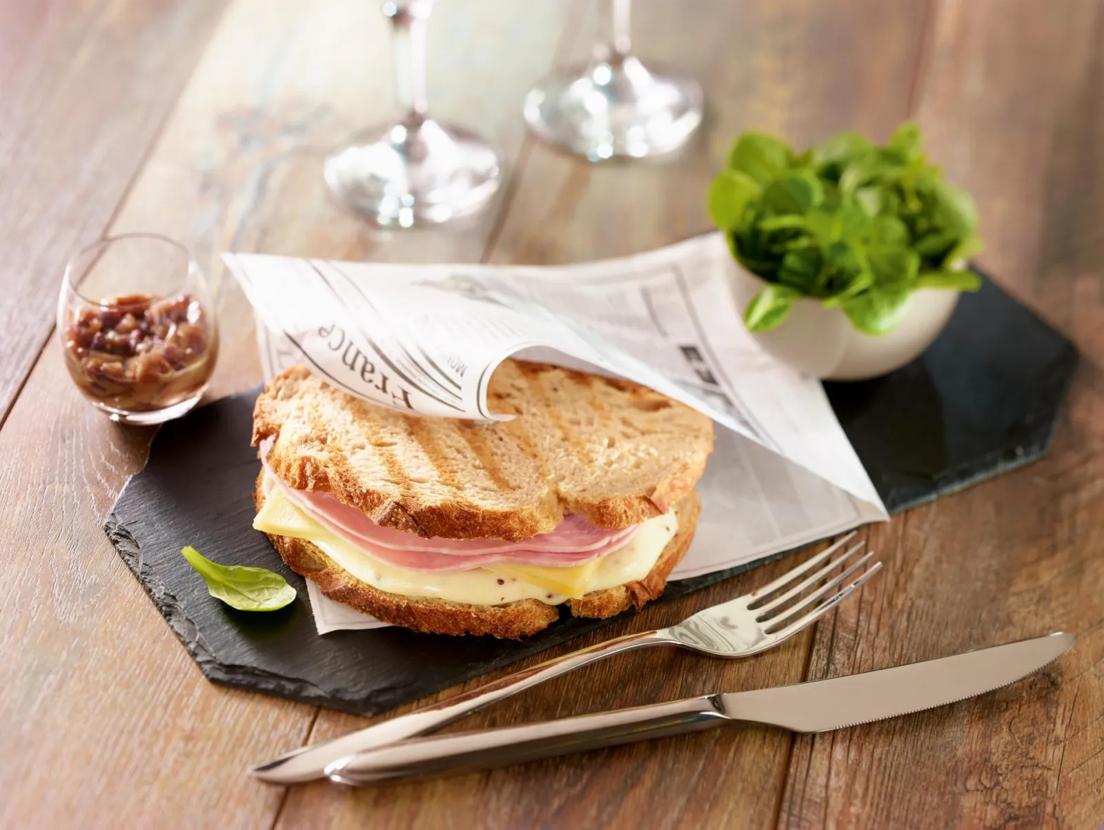 Grilled ham and cheese sandwich served on black slate with fresh green salad, beverage glass, white bread and cutlery in a Bordeaux restaurant