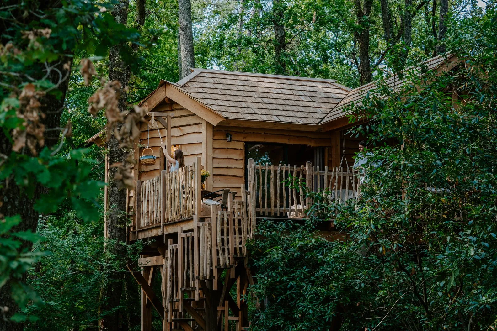 Traditional wooden treehouse cabin with deck and stairs nestled among trees and lush greenery near Bordeaux