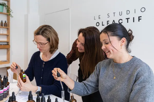 Three women examining fragrance bottles in an olfactory studio in Bordeaux, with rows of scent products displayed on the counter.