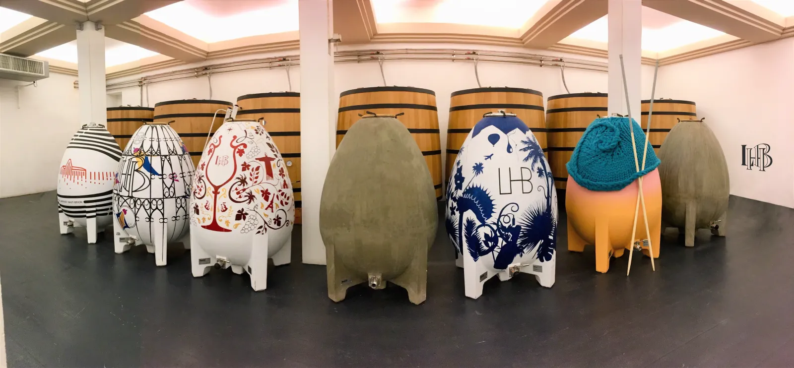 Collection of decorated oak barrels of various sizes and artistic designs arranged in a winemaking cellar at Château Larrivet Haut-Brion in Bordeaux.