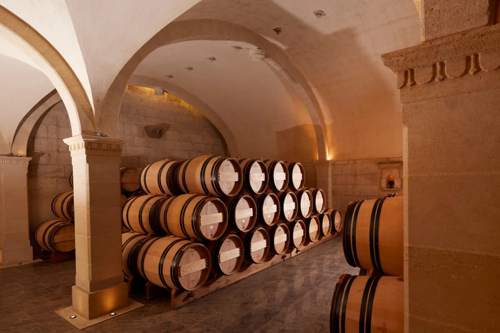 Vaulted wine cellar in the Jacobins Convent in Bordeaux featuring stacked wooden barrels under stone arches