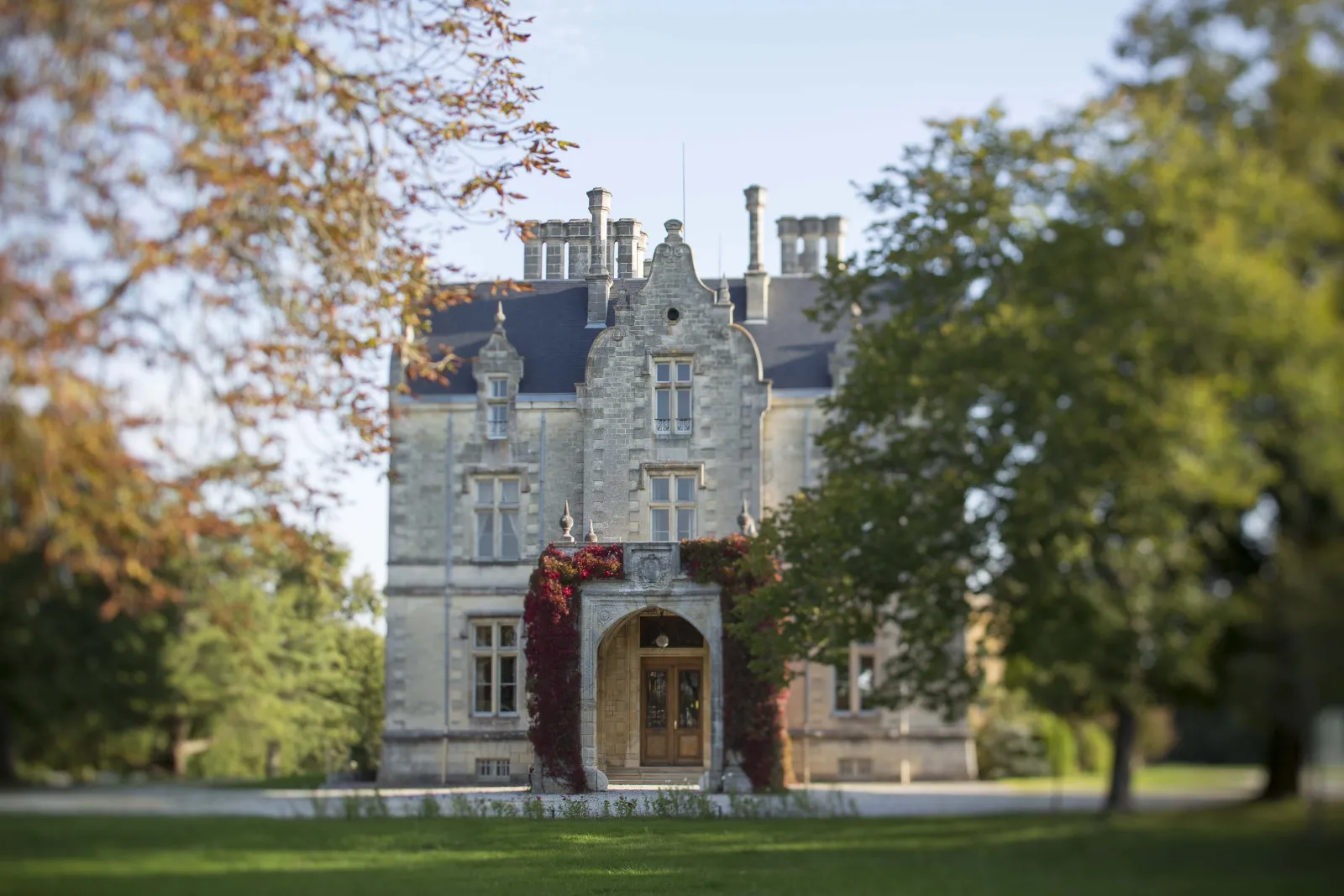 Château Lanessan in Bordeaux, a grand stone mansion with turrets and slate roof, surrounded by autumn foliage and red ivy.