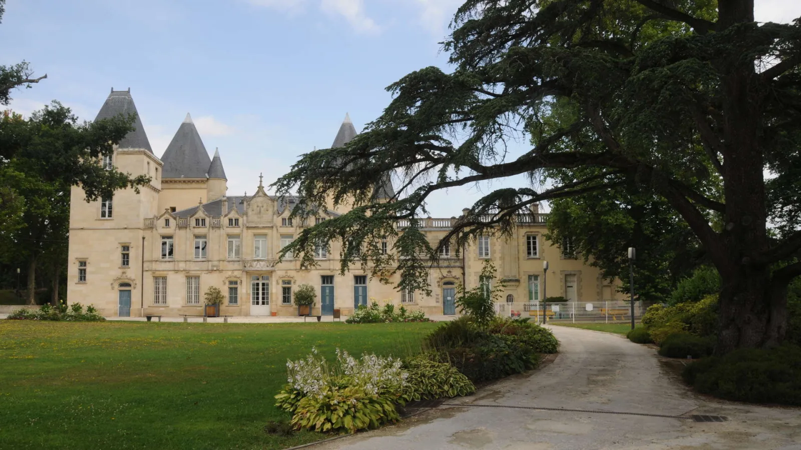 Bois de Thouars château in Bordeaux, a beige stone mansion with turrets surrounded by manicured lawn and ancient trees.