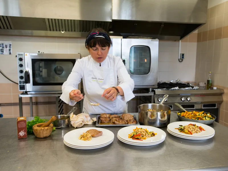 A chef plates dishes in a professional kitchen at Château Kirwan in Bordeaux, with vegetable and protein-based plates visible on the work counter.