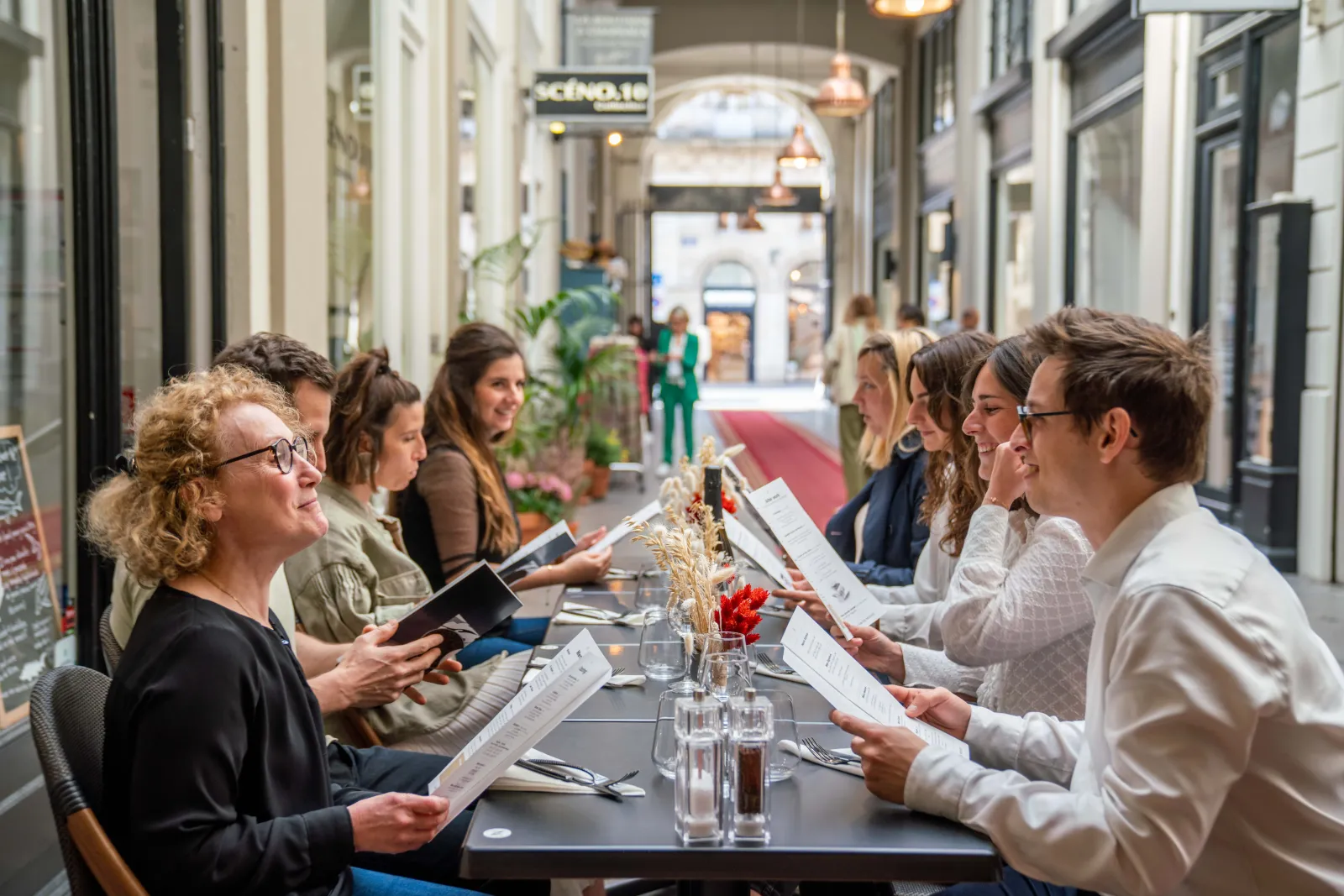 Group of people seated at a table in a covered gallery in Bordeaux, holding menus and glasses of water, during a caviar tasting from Neuvic.