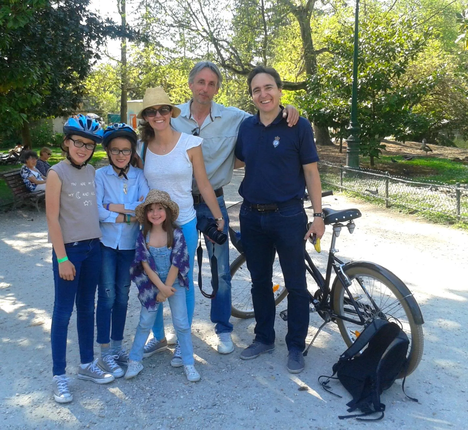 Family of six smiling people posing together in a Bordeaux park, some wearing bike helmets, with bicycles visible nearby.