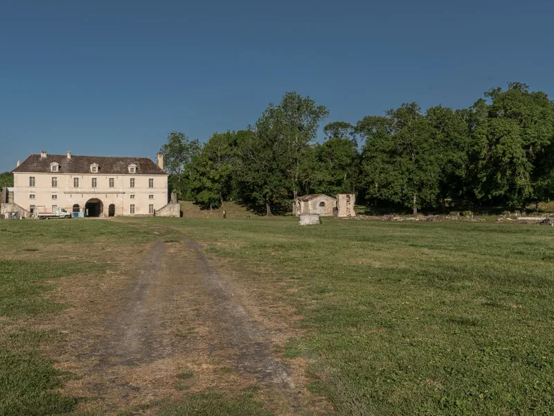 View of Fort Médoc near Bordeaux: a stone building with mansard roof in château style, surrounded by green lawn and trees, reached by a dirt path.