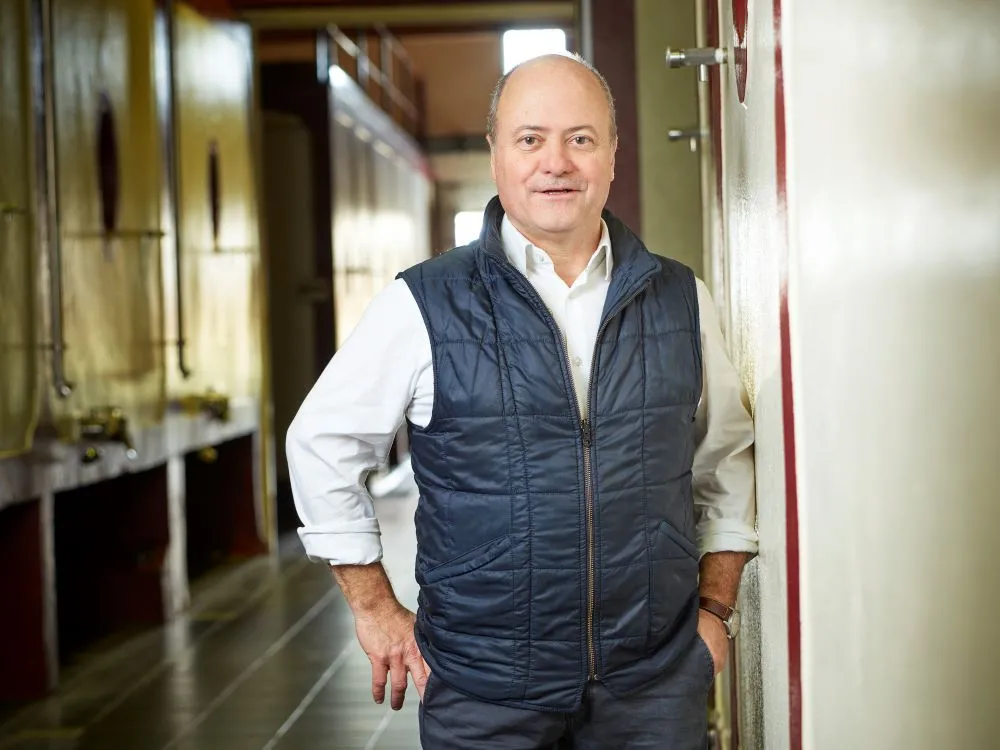 Middle-aged man wearing a dark blue quilted vest and white shirt, standing in a wine cellar corridor at Château Grand Corbin-Despagne in Bordeaux.