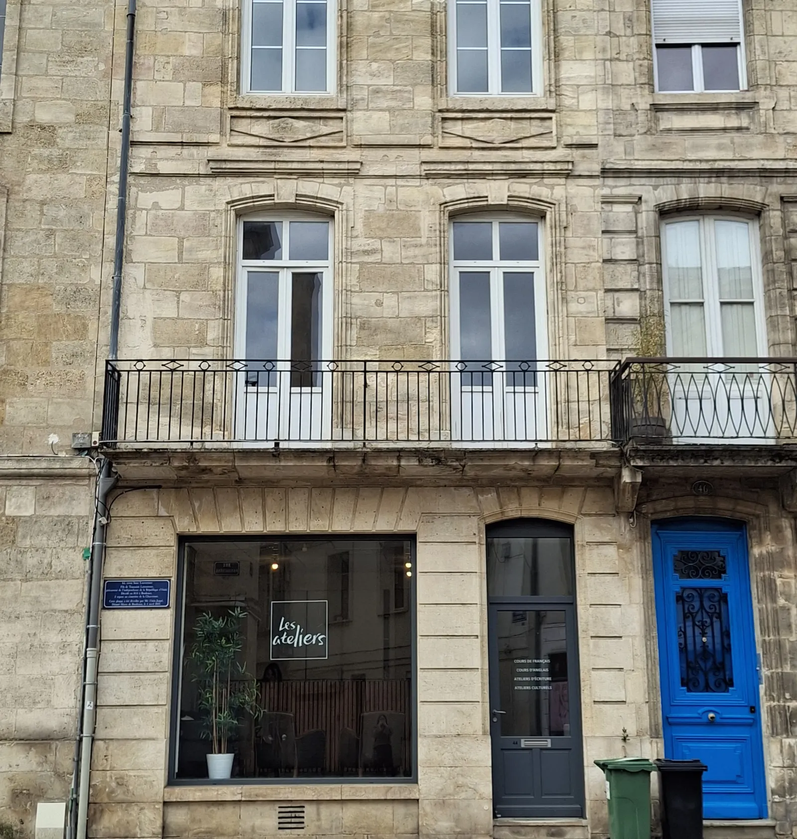 Haussmann-style building facade in Bordeaux featuring the FL workshops storefront on the ground floor, a blue door, and a first-floor balcony