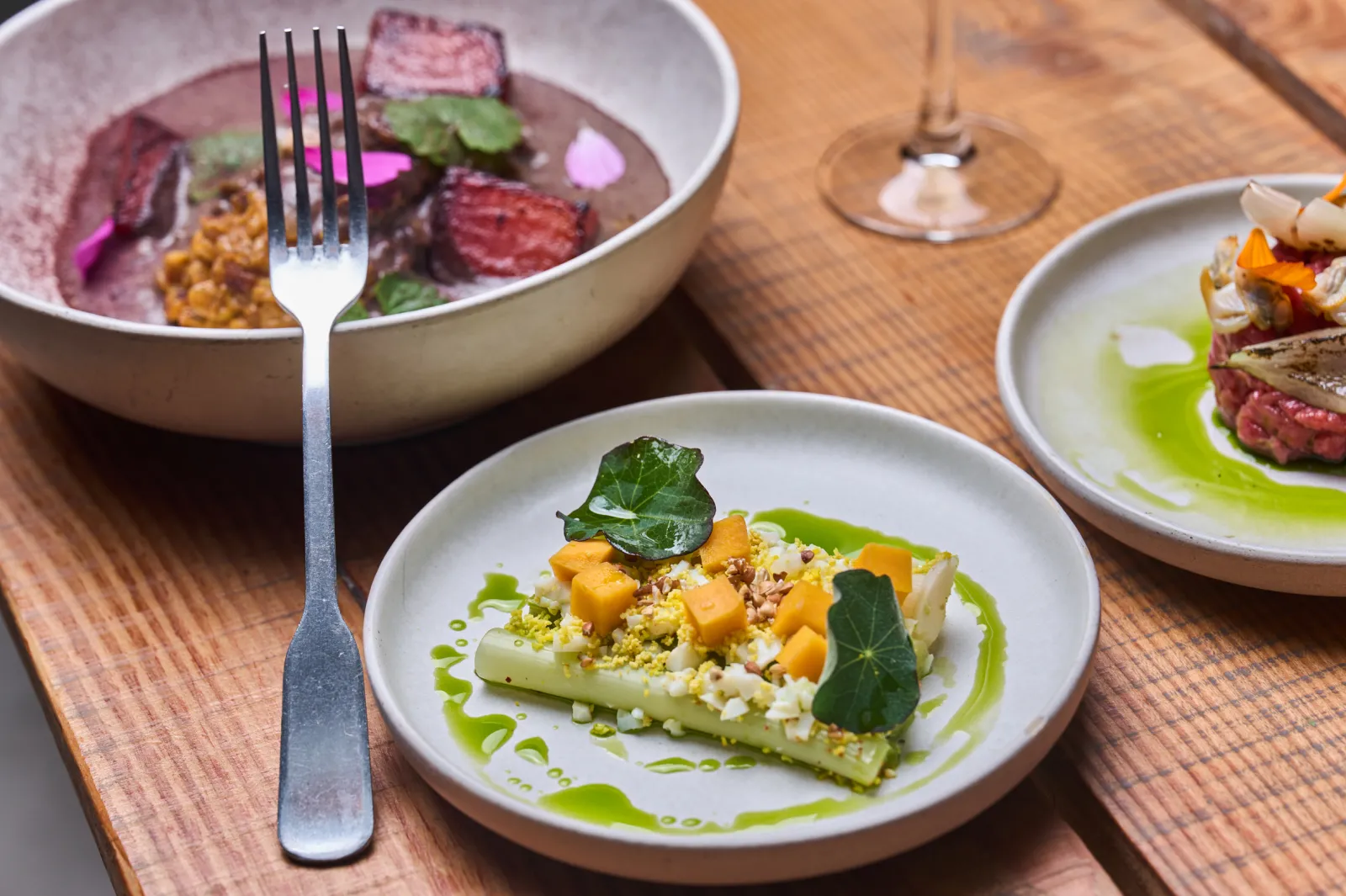 Gourmet plate featuring a stuffed vegetable with colorful vegetables and green sauce, accompanied by three other refined dishes on a wooden table in a restaurant.