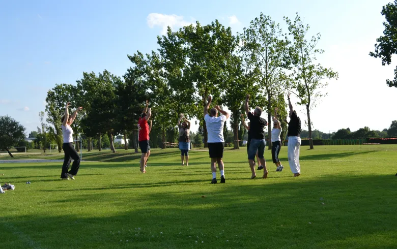 Group of people doing fitness exercises with jumping movements in a green park at Domaine du Pinsan in Bordeaux, surrounded by trees.