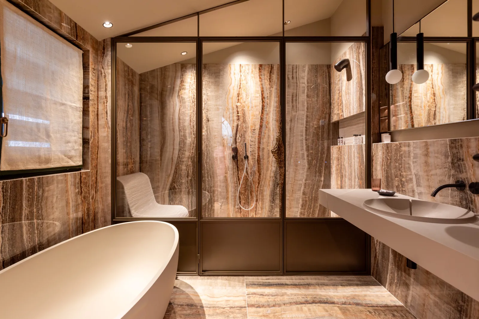 Modern bathroom at Yndo Hotel in Bordeaux featuring a white bathtub, walk-in shower, minimalist sink, and warm travertine marble wall cladding
