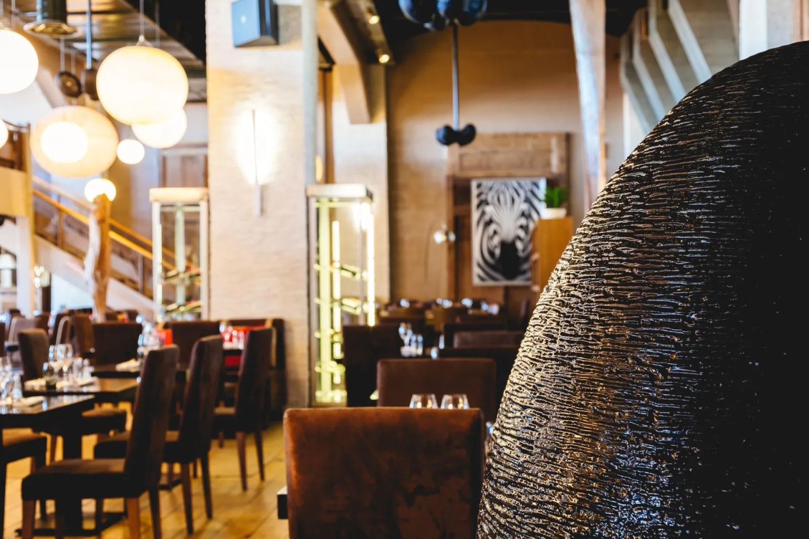 Interior of Café Maritime in Bordeaux featuring brown leather seating, round hanging lights, minimalist décor and zebra artwork on the wall