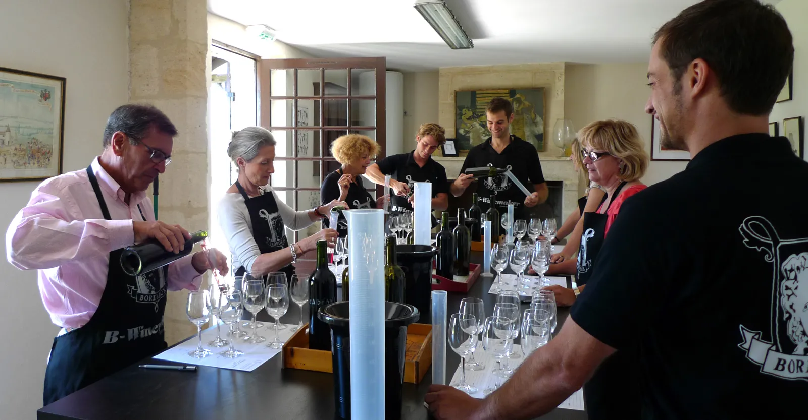 Wine tasting session in Bordeaux with a sommelier presenting wines to a group of participants around a table with glasses and bottles.