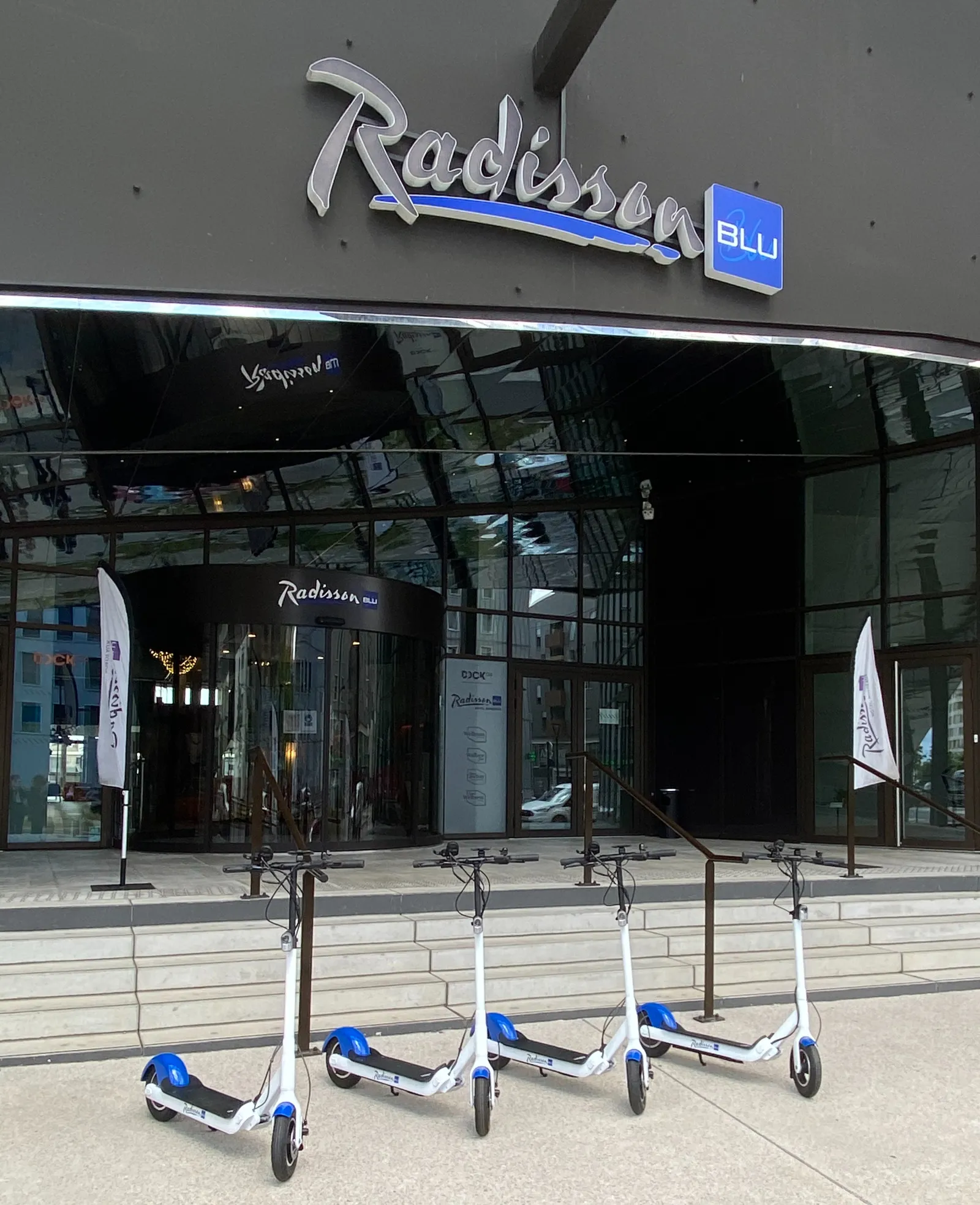 Front view of Radisson Blu Hotel Bordeaux featuring the illuminated sign and four blue and white electric scooters parked in front of the entrance