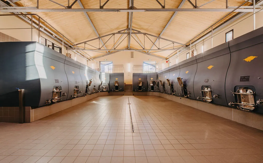 Modern winery interior at Château Rol Valentin in Bordeaux featuring stainless steel fermentation tanks arranged symmetrically beneath a wooden ceiling with metal framework