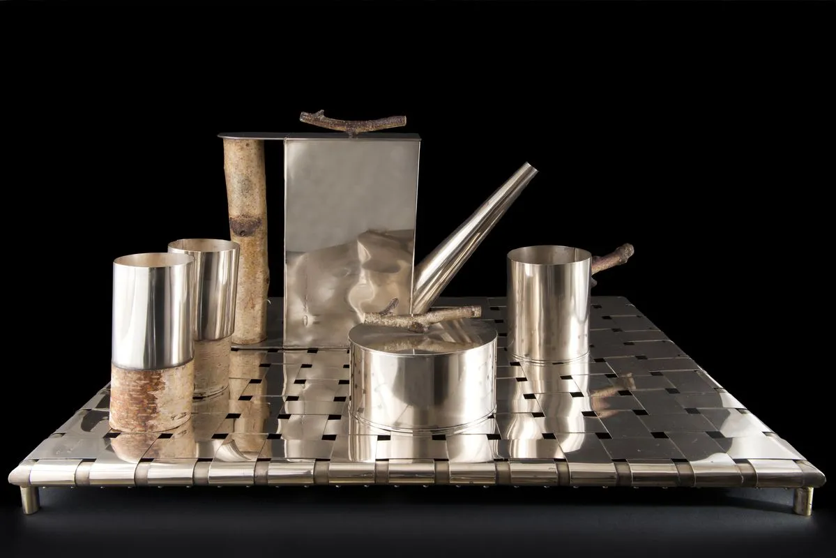 Silver-plated tea service with multiple pieces including a teapot, milk pitcher, cups, and spoon with natural wooden handles, displayed on a perforated metal tray.