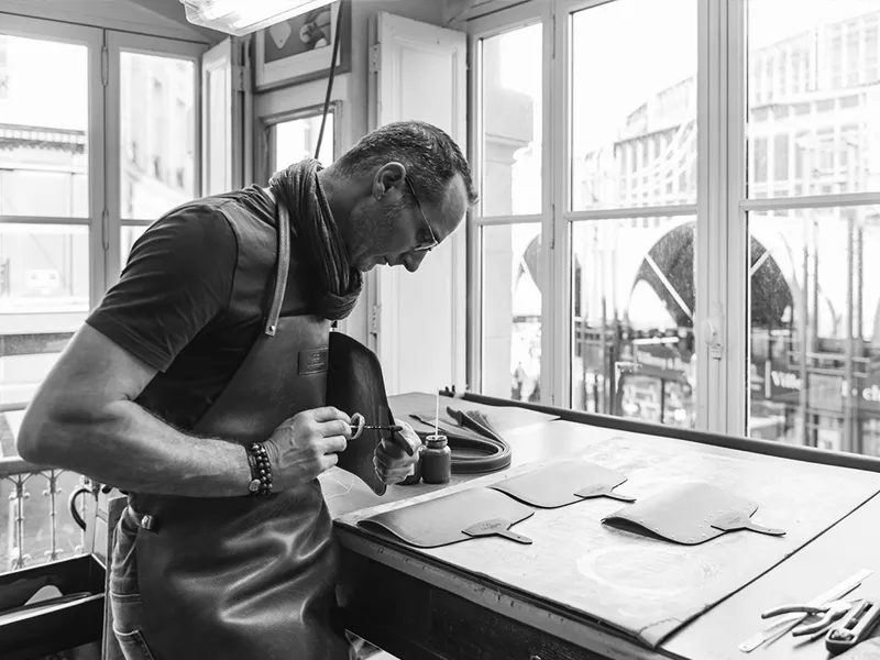 Leather craftsman working at his workbench in a Bordeaux workshop, with city views in the background
