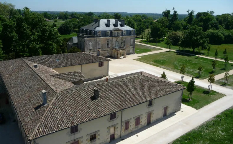 Aerial view of Domaine de Beauval in Bordeaux featuring an 18th-century château with mansard roof, farm buildings with tile roofs, a paved driveway, and manicured parkland with scattered trees.