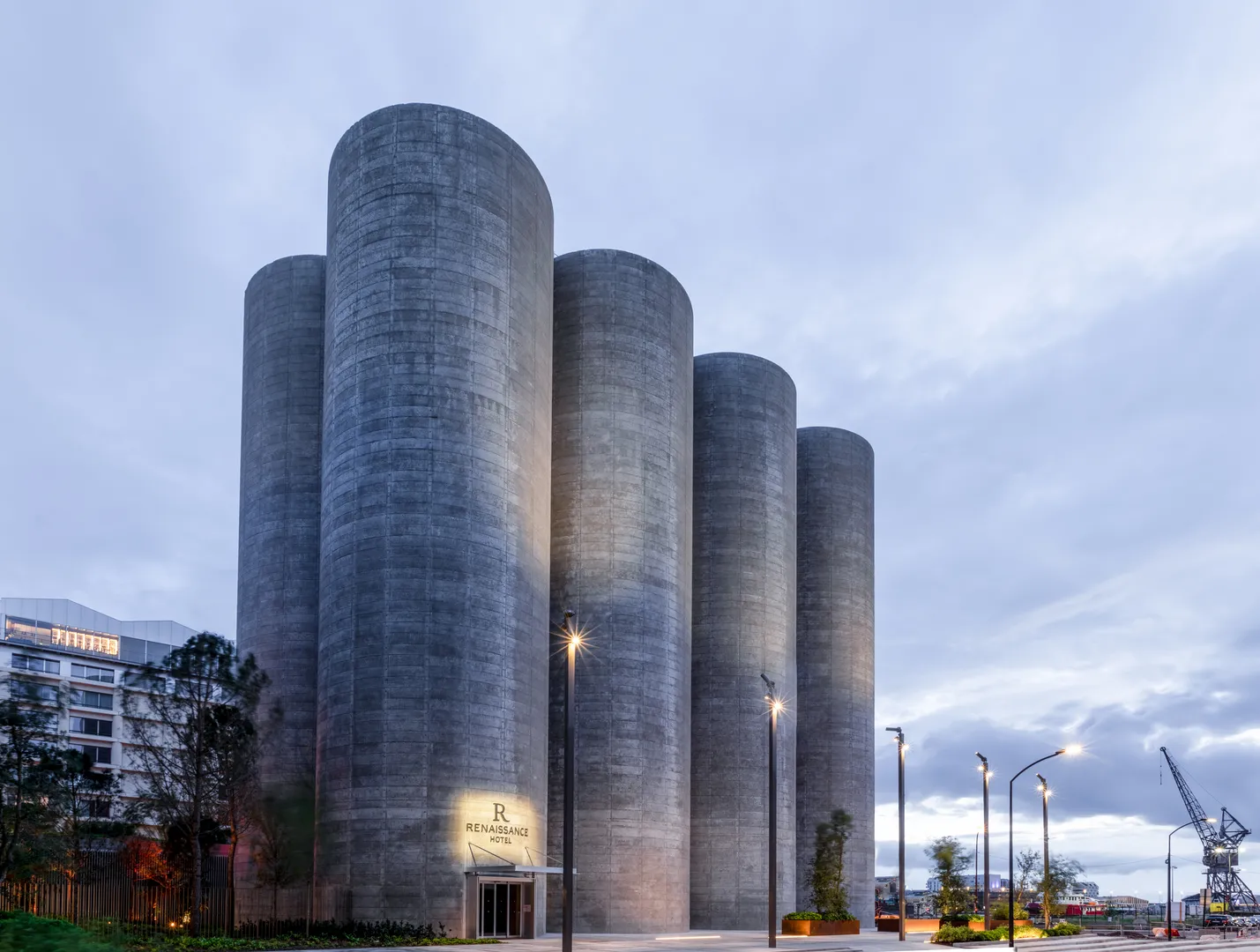 Facade of Renaissance Bordeaux Hotel, a modern architectural building consisting of five gray concrete cylinders aligned together, located in Bordeaux's harbor at dusk.