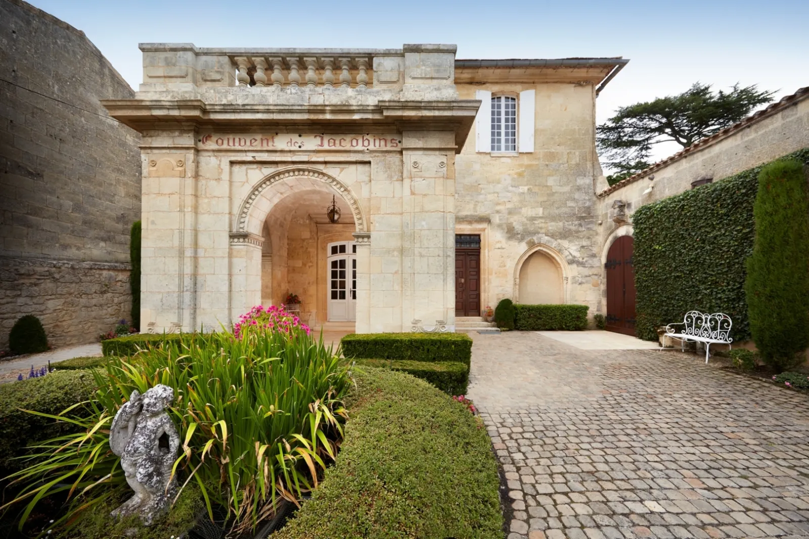 Inner courtyard of the Jacobins Convent in Bordeaux featuring stone facade, Romanesque arch, manicured gardens and pink flowers
