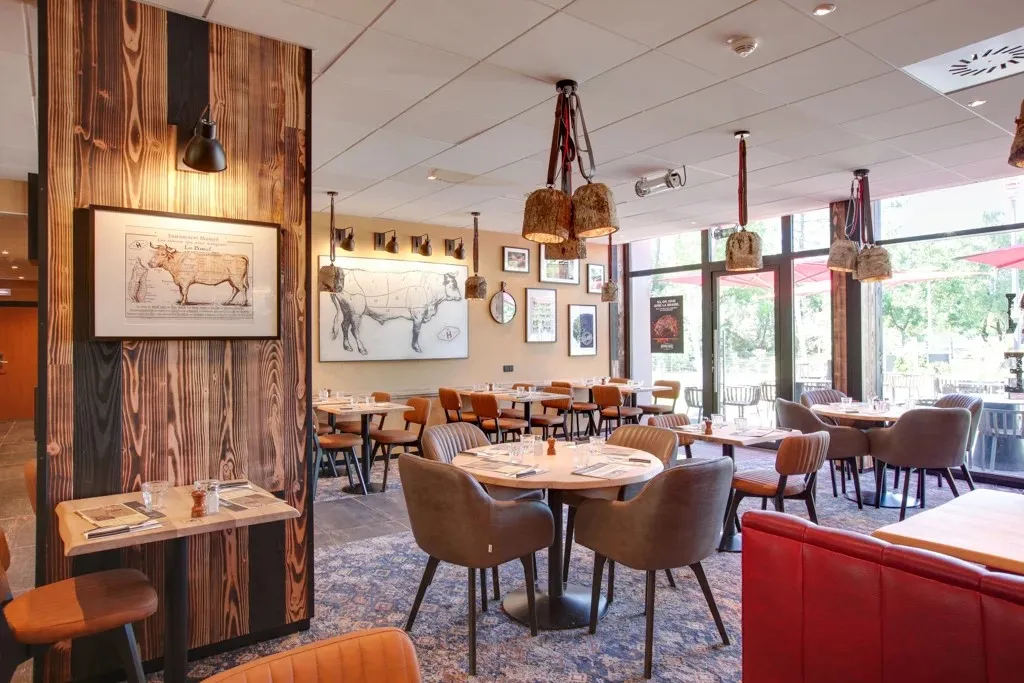 Interior of Hippopotamus restaurant in Bordeaux featuring round tables, brown chairs, wooden wall decor with anatomical animal illustrations, and bright windows