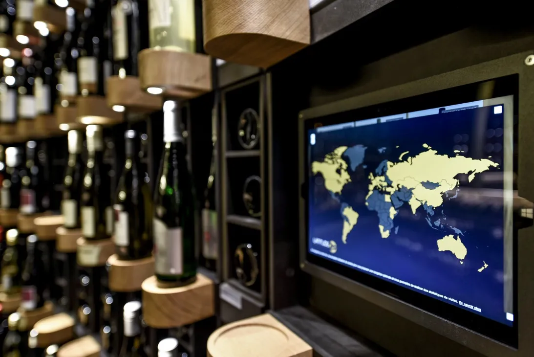 Wine bar interior with world map displayed on screen, wine bottles on wooden shelves with ambient lighting