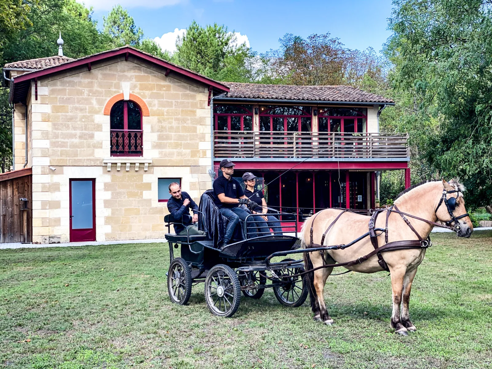 Horse-drawn carriage ride in front of Château Léognan in Bordeaux, with visitors aboard and a stone building with Bordeaux architectural features in the background.