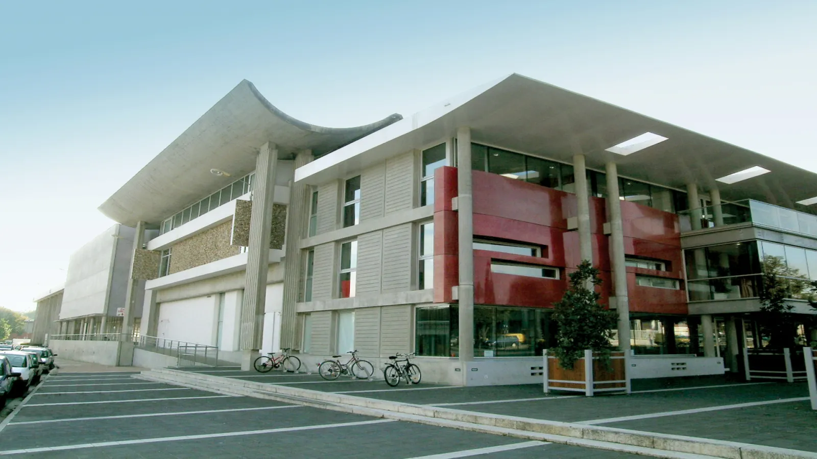 Modern building Le Carré in Saint-Médard-en-Jalles, Bordeaux, featuring contemporary concrete architecture with red accents, large columns, and bicycle parking.