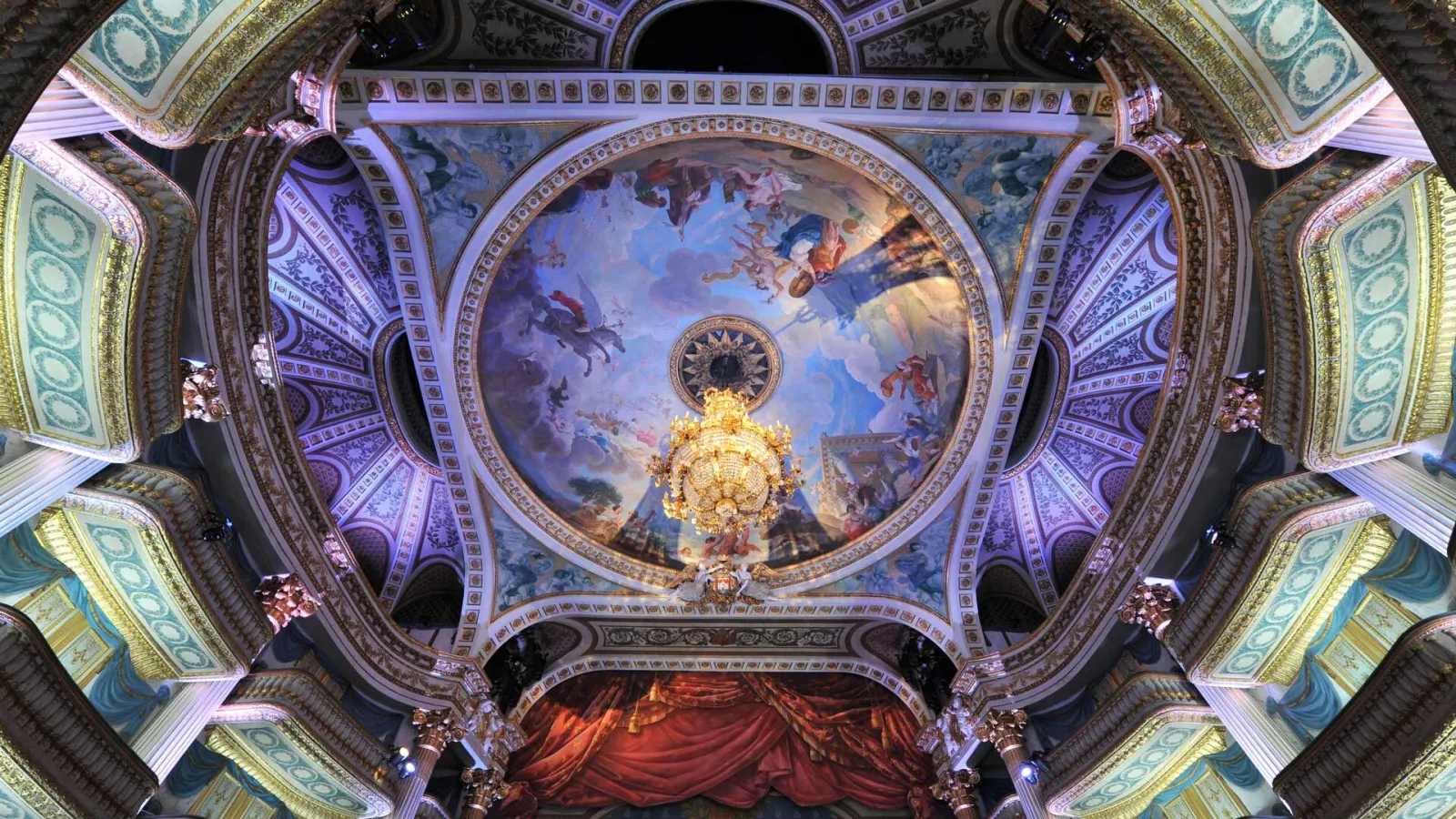Ceiling view of the Grand Theatre of Bordeaux featuring an ornate circular dome with mythological frescoes, golden chandeliers, and rococo blue and gold decorations.