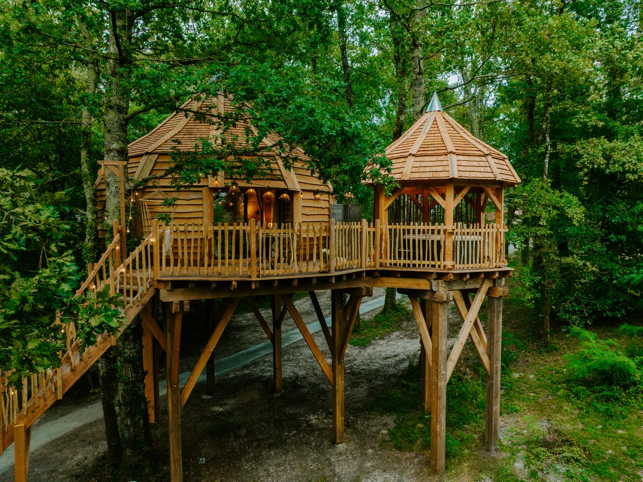 Elevated wooden treehouse structure in a forest with two conical towers and connecting walkway, located in Bordeaux.