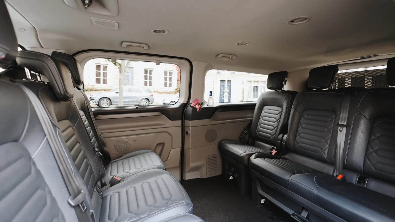Spacious interior of a minibus featuring black and gray leather seats, panoramic windows, and ceiling with recessed lights, in a Bordeaux transportation context.