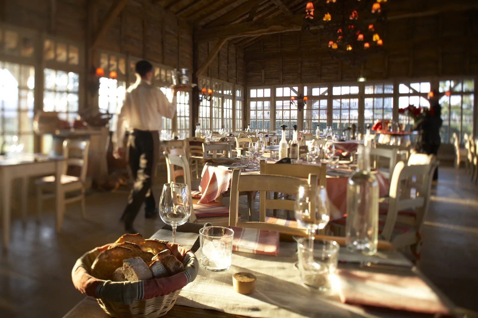 Elegant dining room with set tables, glassware and bread baskets, flooded with natural light from large windows, in Bordeaux.