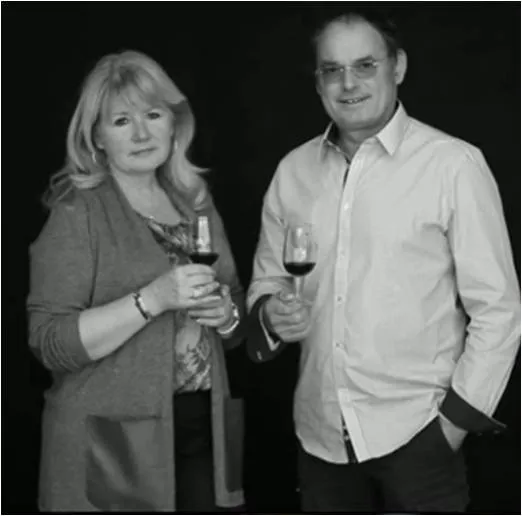 A man and woman pose together in black and white, each holding a wine glass against a black background at Château Léognan in Bordeaux.