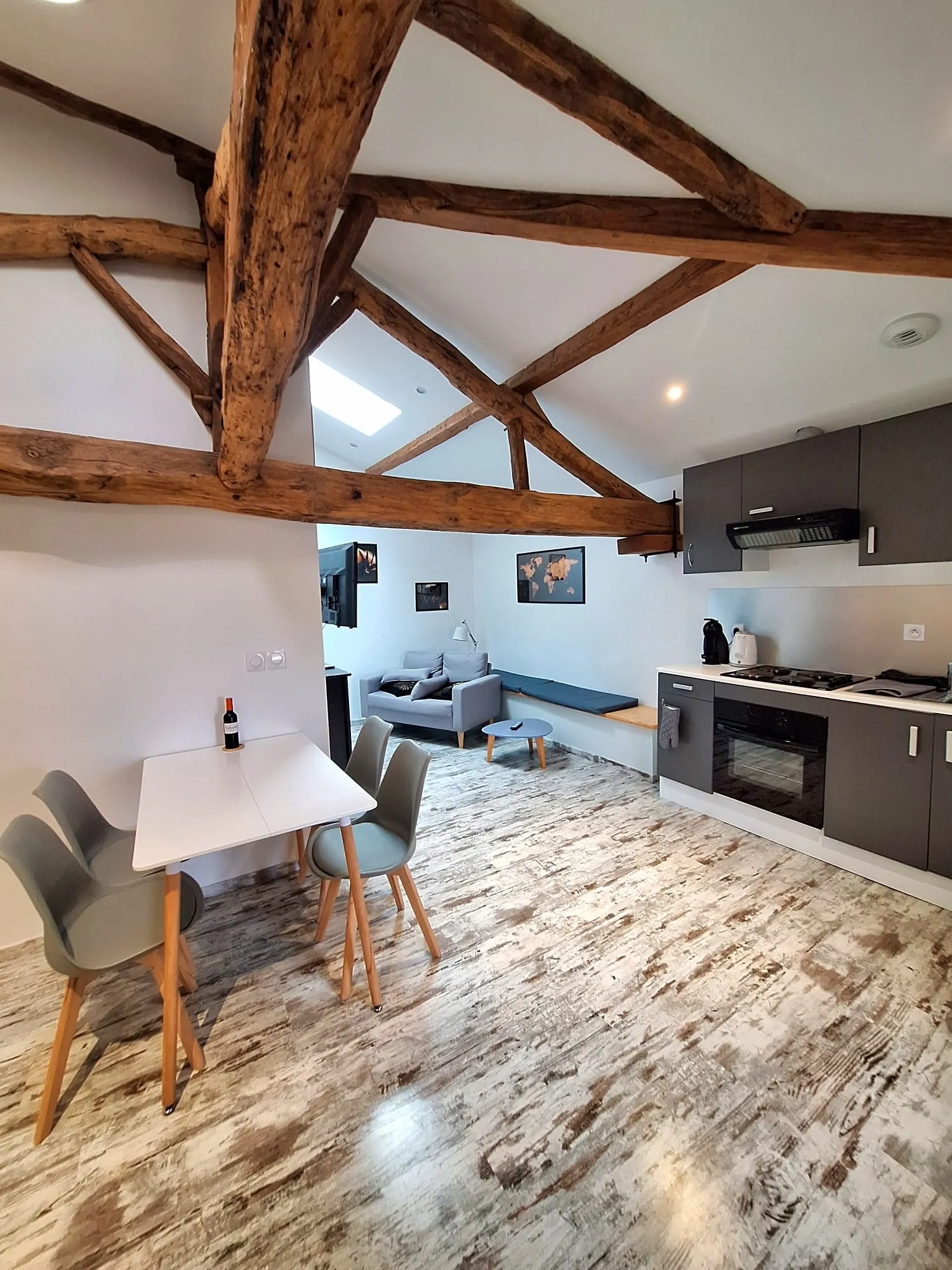Merlot Studio at Château Pierre de Montignac in Bordeaux: modern interior with exposed wooden beams, equipped kitchen, white dining table, blue sofa and wood-effect tile flooring