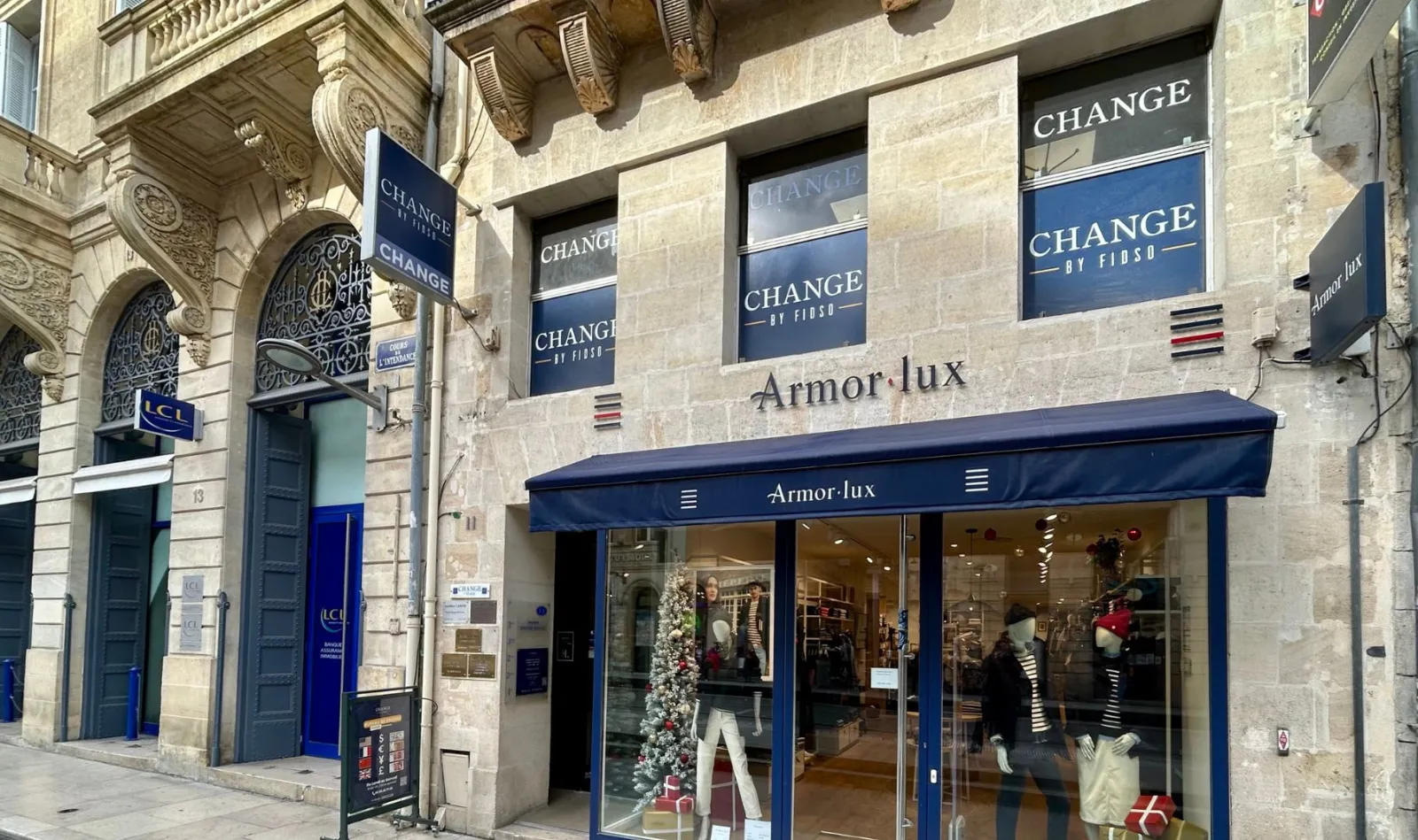 Storefront of Armor·lux shop on rue de l'Intendance in Bordeaux, featuring blue 'Change' signage, large display windows with clothing, and located in a historic stone building.