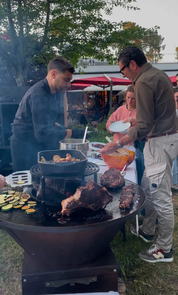 Three men cooking around a large outdoor grill at an event in Bordeaux, with grilled meats and vegetables being prepared.