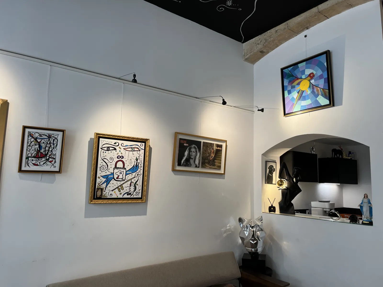 Interior of SP Pour toi gallery in Bordeaux featuring multiple artworks displayed on white walls, including abstract and figurative paintings, a metal sculpture, a digital screen, and a wall niche with various objects.