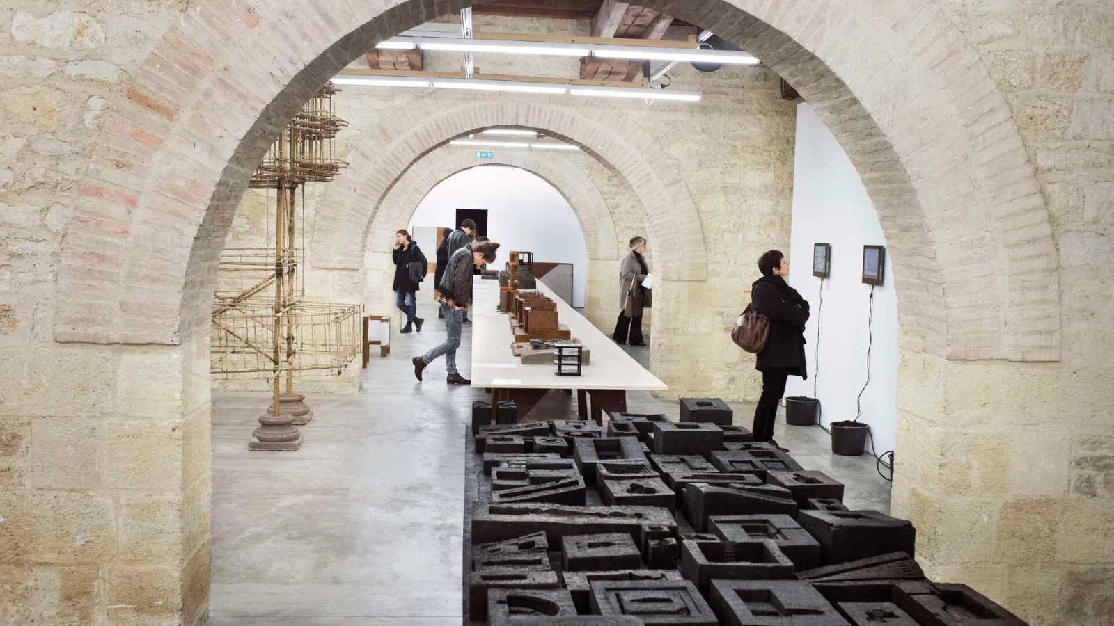 Vaulted underground gallery at Arc en rêve in Bordeaux featuring a modern architecture exhibition with black scale models on the floor, white display panels on walls, and visitors exploring the installations.