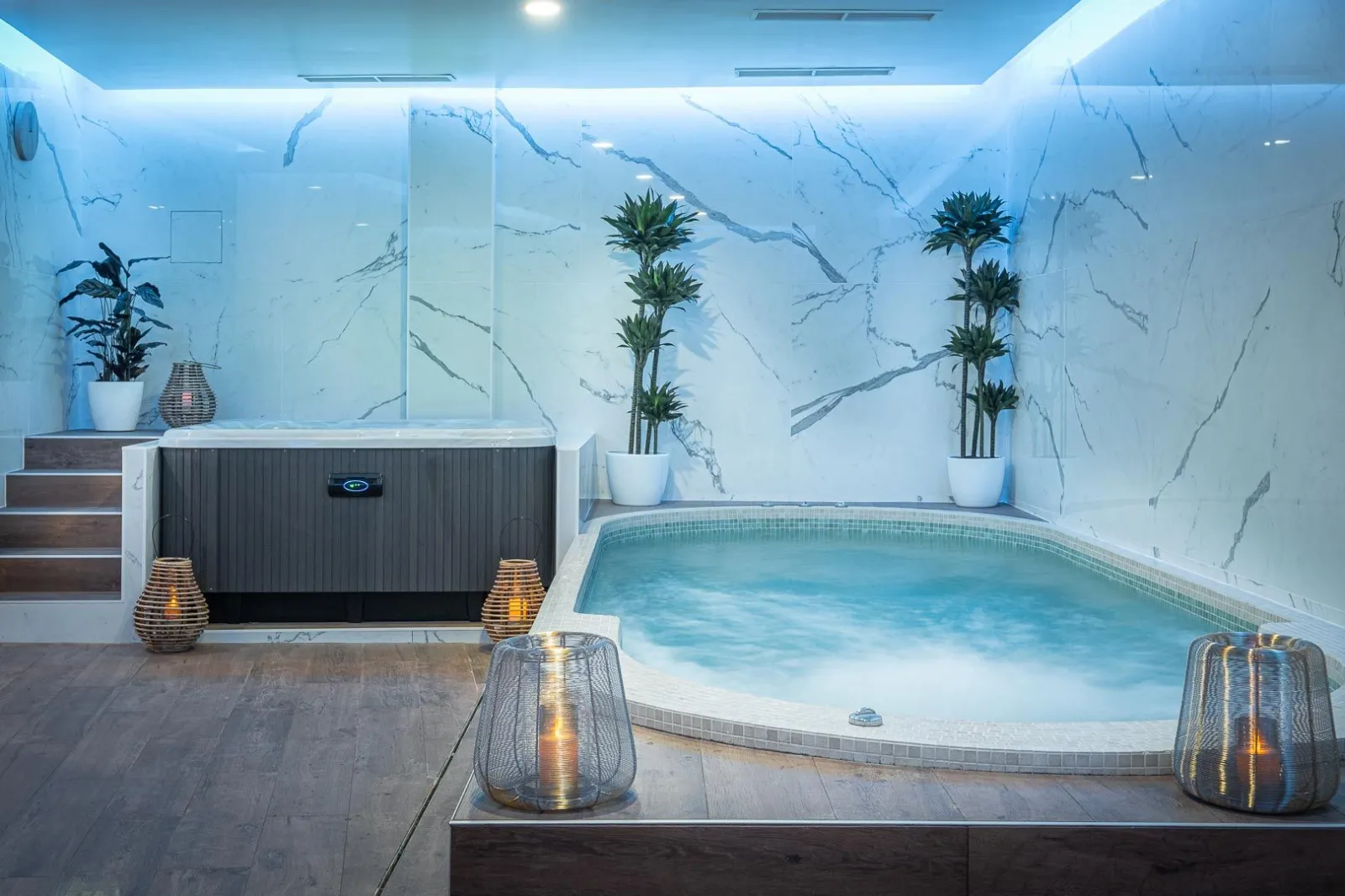Upscale indoor spa featuring a heated turquoise swimming pool, white veined marble walls, potted palm trees, illuminated hot tubs, and contemporary furnishings at Palais Gallien Hotel & Spa in Bordeaux.